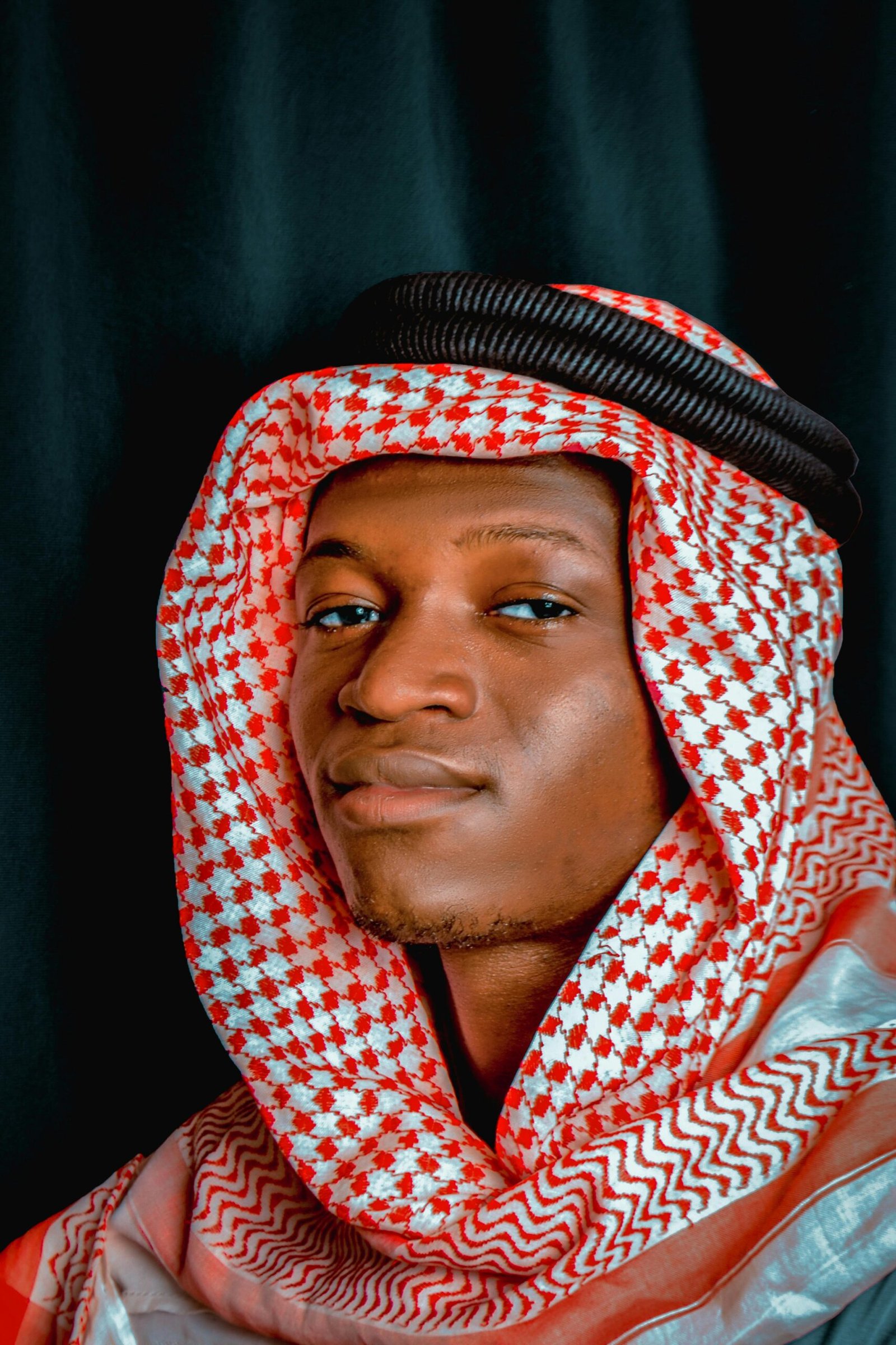 Close-up portrait of a man wearing traditional keffiyeh against a black background.